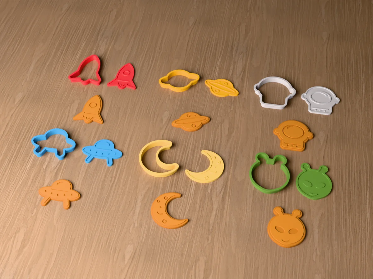 3D render of six 3D-printed space cookie cutters with their stamps and a golden stamped cookie in front of each: rocket, ringed planet, astronaut helmet, flying saucer, crescent moon and alien