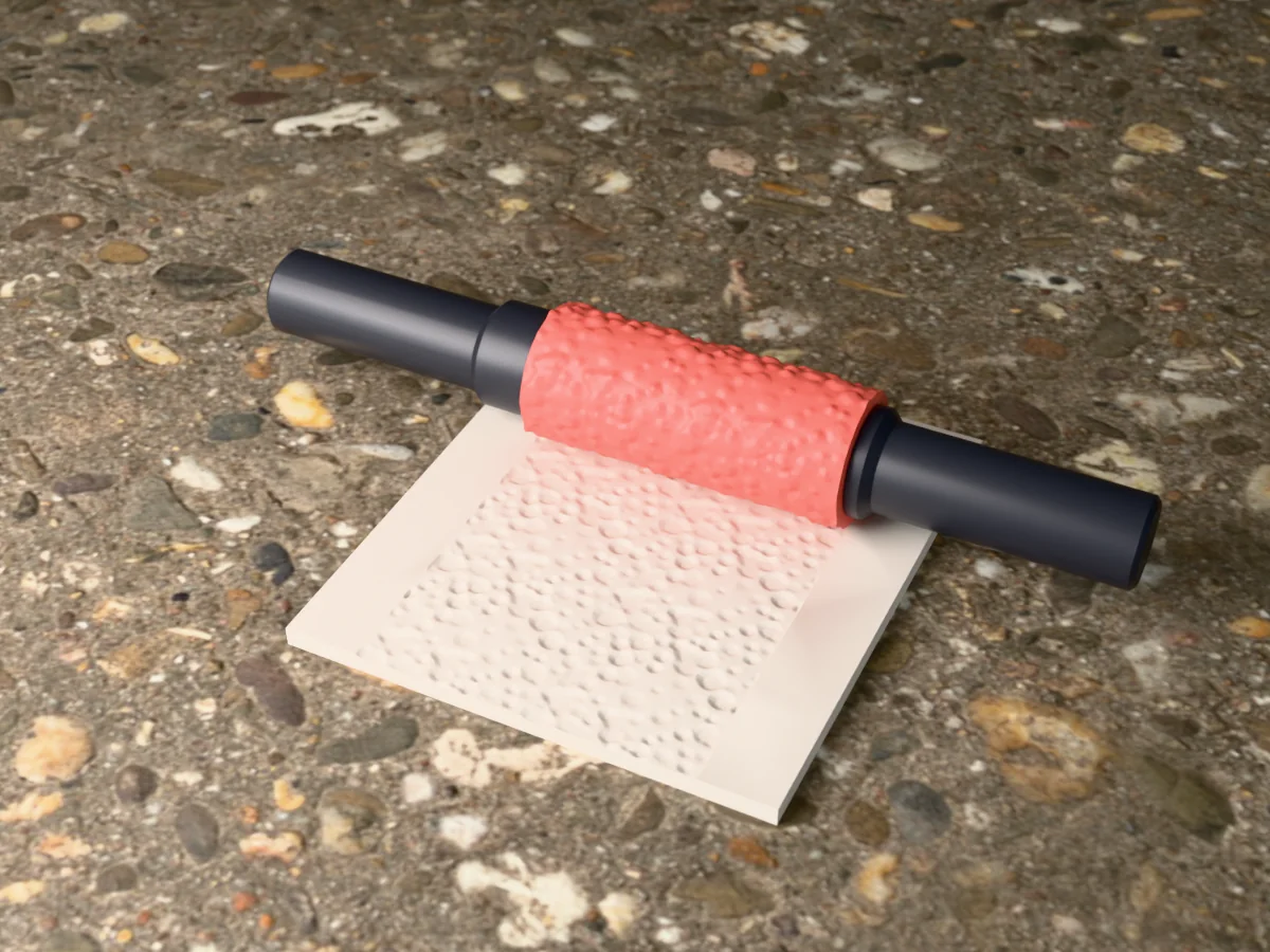 3D render of the printed terrazzo textured rolling pin, its patterned sleeve between two dark handles, resting on a slab of clay it has pressed with a terrazzo