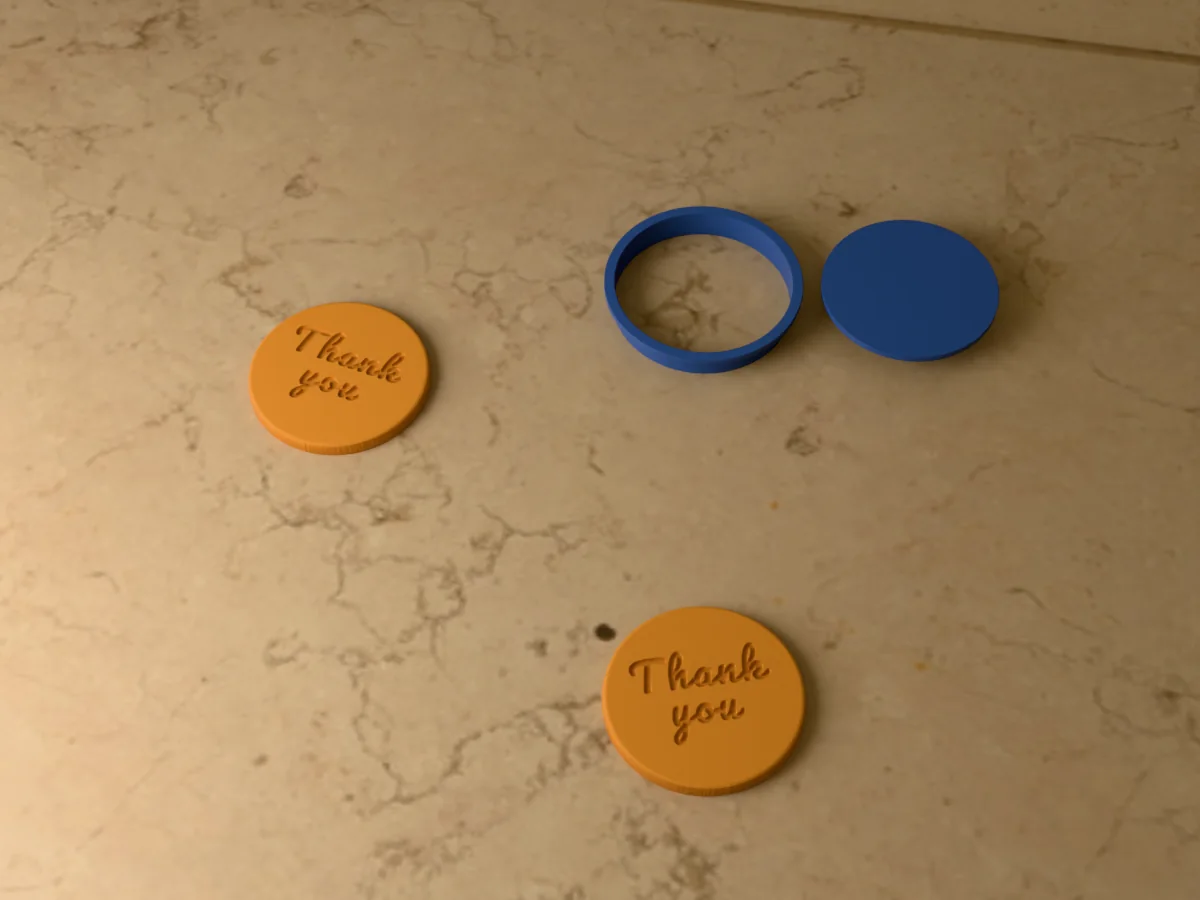 3D render of a navy blue 3D-printed round cookie cutter and Thank you stamp next to two golden baked cookies with Thank you pressed in