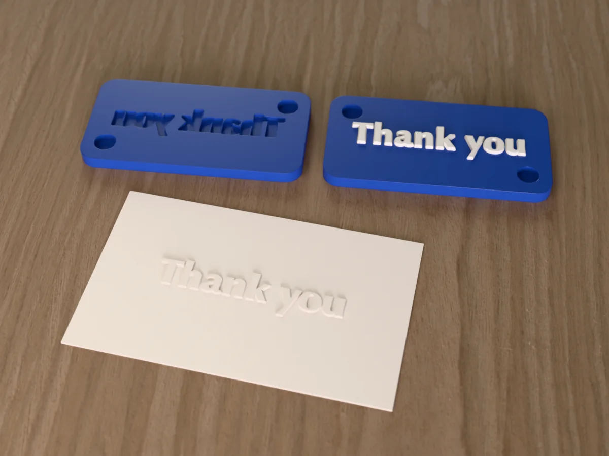 3D render of the printed thank you embosser, its two plates side by side, with the raised die and the matching cavity, next to a card embossed with its mark