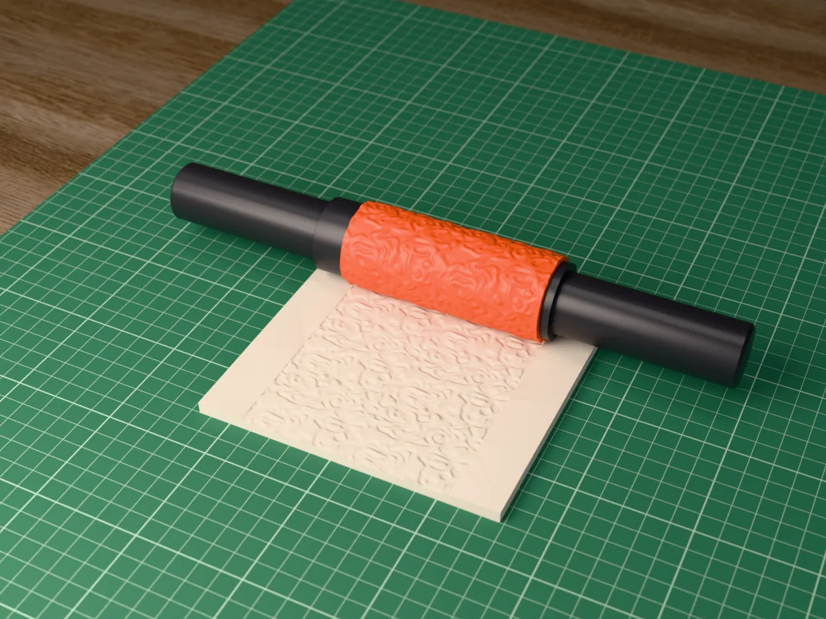3D render of the printed topographic map textured rolling pin, its patterned sleeve between two dark handles, resting on a slab of clay it has pressed with topographic contour lines