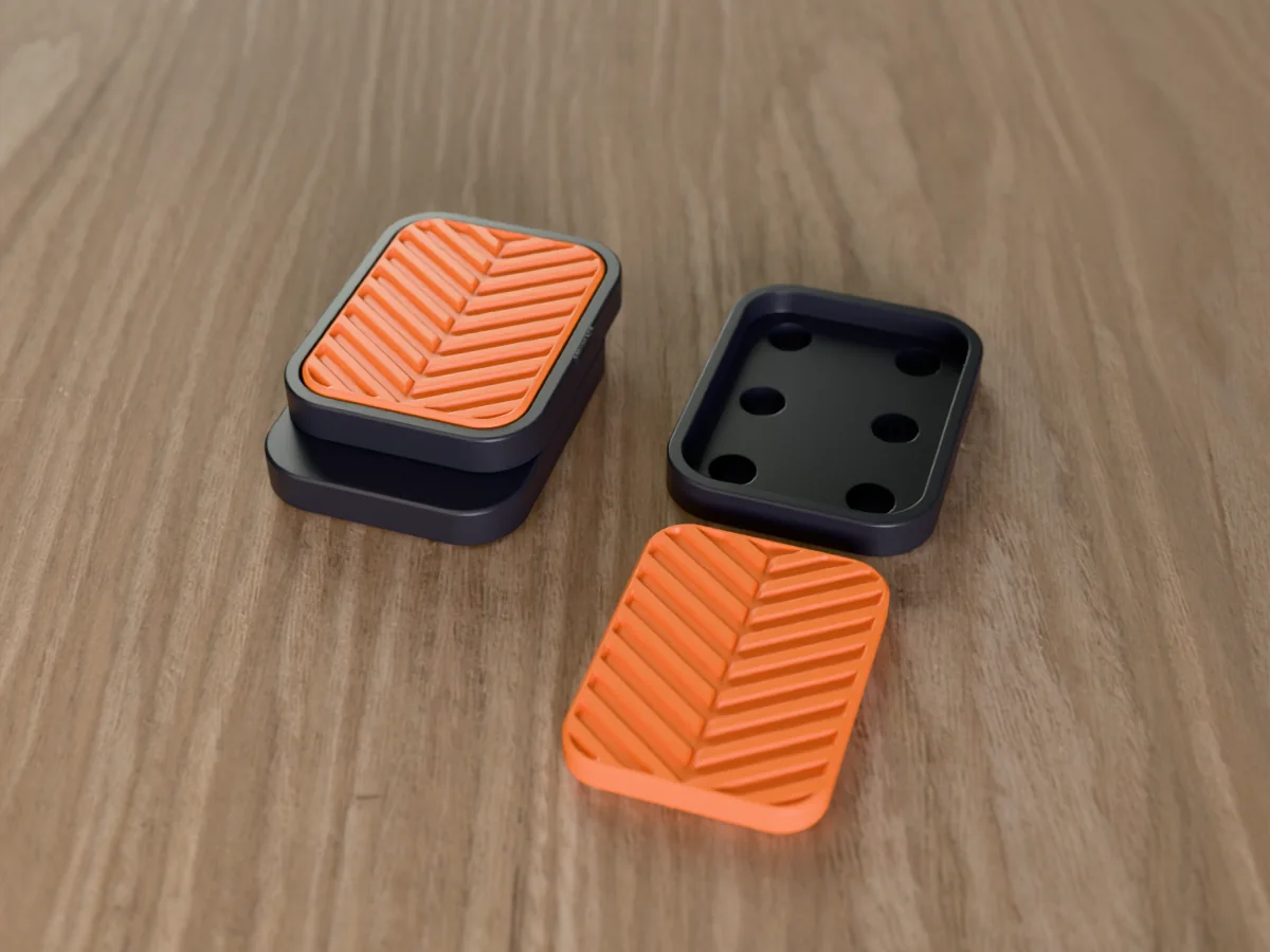 3D render of a black and orange 3D-printed magnetic fidget slider with a tyre tread texture, assembled, next to a spare plate and insert