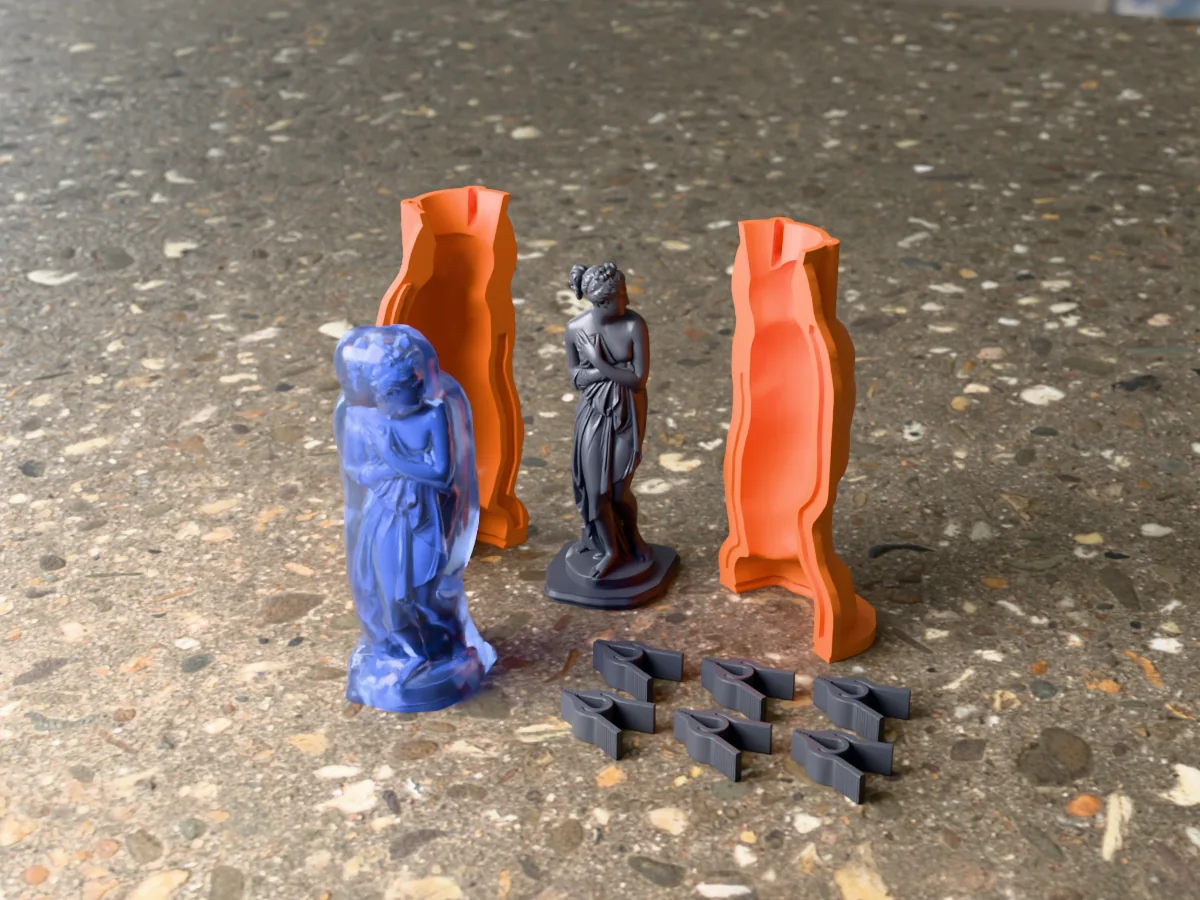 3D render of the Venus Italica master on its printed charcoal base between the two orange hugging-shell halves, with the six printed clamps and the cured translucent blue silicone mold in front