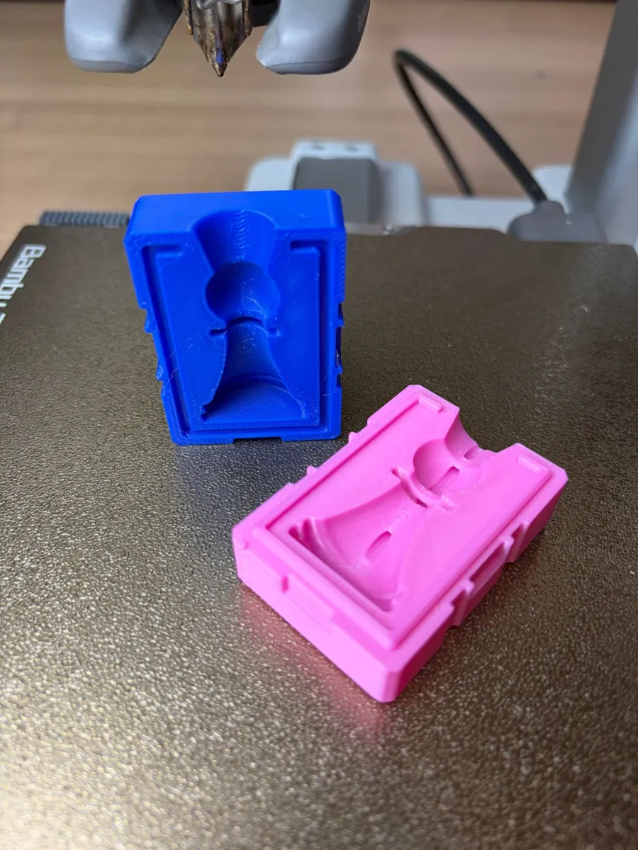 The two printed halves of the chess pawn mold, blue and pink, opened on the print bed with the pawn cavity showing