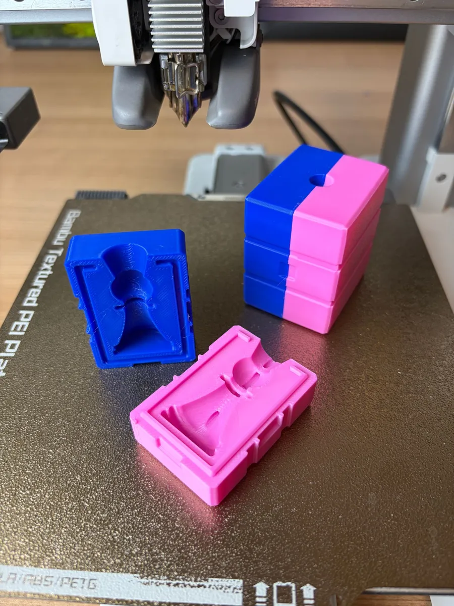 Both open halves of the printed chess pawn mold next to a stack of closed blue and pink molds with the pour hole on top