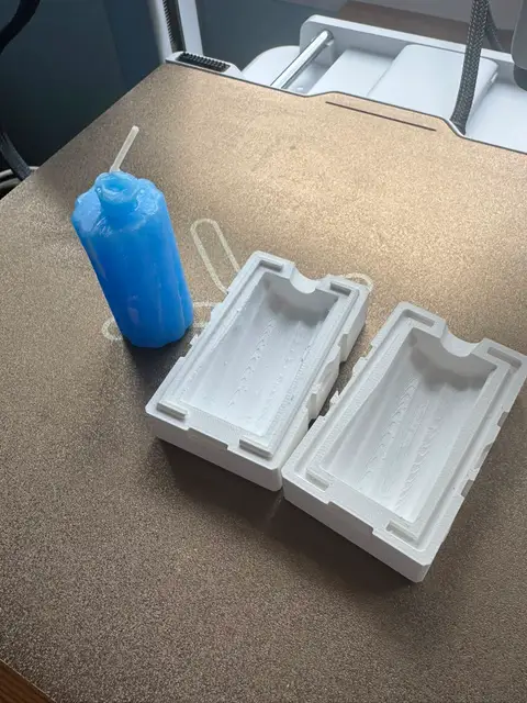 A blue pillar candle beside the 3D-printed two-part mold it was cast in.