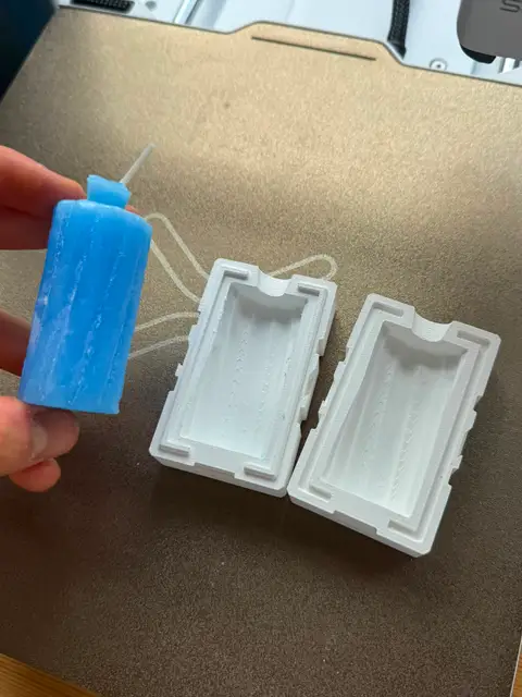 A cast wax candle next to the 3D-printed two-part mold it came from.