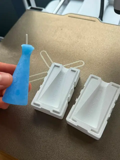 A poured wax candle beside the 3D-printed two-part mold it came from.