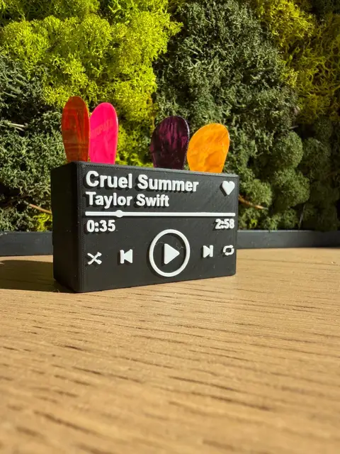 A 3D-printed now-playing music card stand holding four guitar picks, made with the Guitar pick holder tool.
