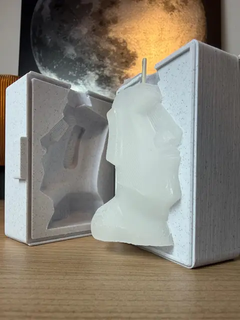 A printed two-part candle mold opened, with the finished white wax candle standing in front of it