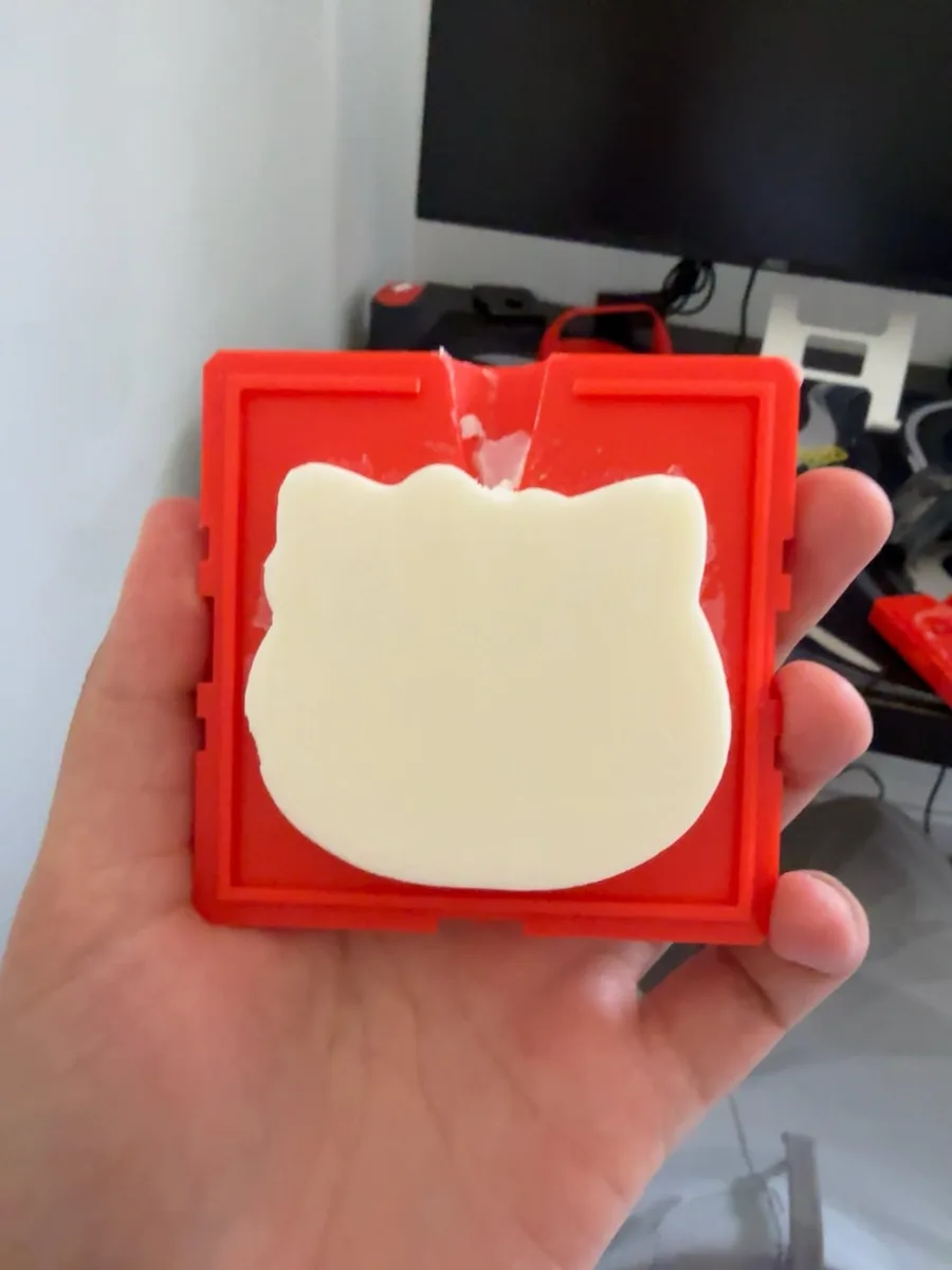 A cat-face wax candle still sitting in the red printed two-part mold it was cast in