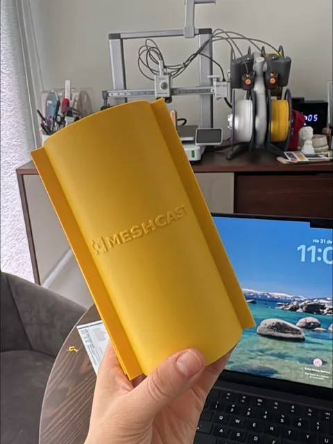 One half of a large gold 3D-printed silicone formwork, the MESHCAST logo embossed across its outer wall, held up in front of the printer that made it.