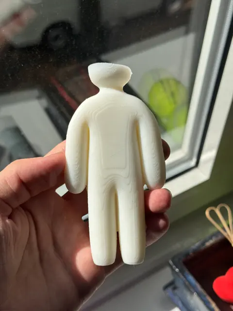 The back of a wax figure candle held in one hand, the printed mold's fine layer lines picked up as contour rings across the wax.