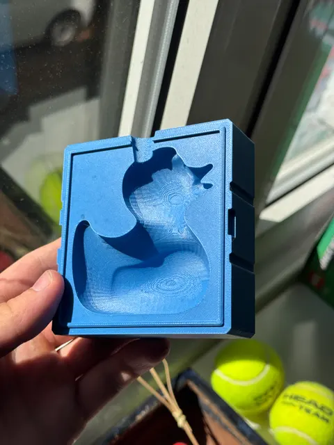 One half of a blue 3D-printed two-part rubber-duck mold held up to the light, showing the duck cavity, the alignment keys along the rim and the pour funnel notch.