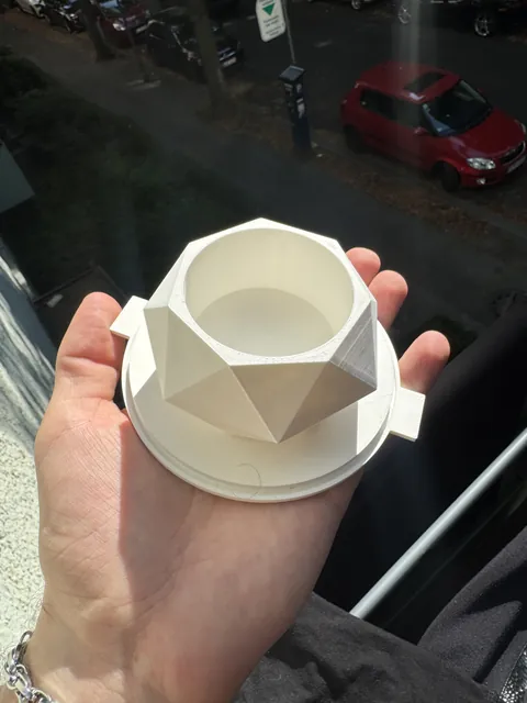 A white 3D-printed faceted plant pot master tipped forward in one hand, showing the hollow round cavity inside and the two locating tabs on its base plate.