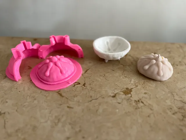 A pink 3D-printed two-part mold and its pan de muerto master, next to the white cast shell and the finished candle.