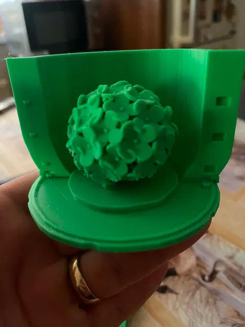 A green 3D-printed two-part hydrangea mold held open, with the printed flower-ball master still sitting on its base plate.