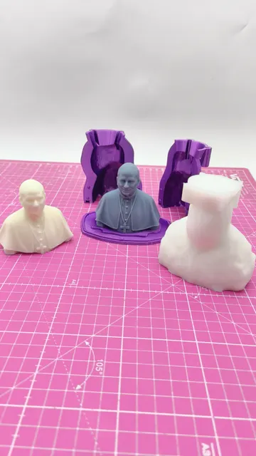 Two purple two-part printed molds behind a grey pope bust on its printed base, with a cream cast on one side and the white silicone negative on the other. Made by @punto3dperu.