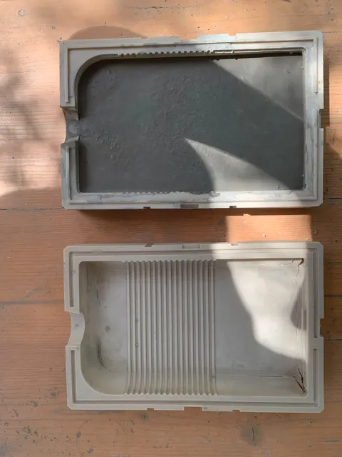 Beide Hälften einer gedruckten Game-Boy-Form auf einer Holzbank, in einer liegt noch der graue Zementguss