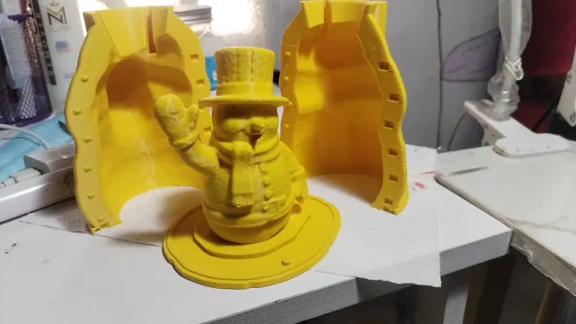 A yellow two-part printed mold standing open behind the waving snowman master it was built around.