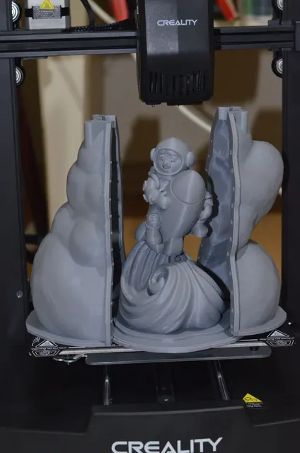 A grey 3D-printed figure of a child in a space helmet riding a rocket on a swirling wave, standing on the print bed between the two open halves of its mold. Made by @zevra.home.