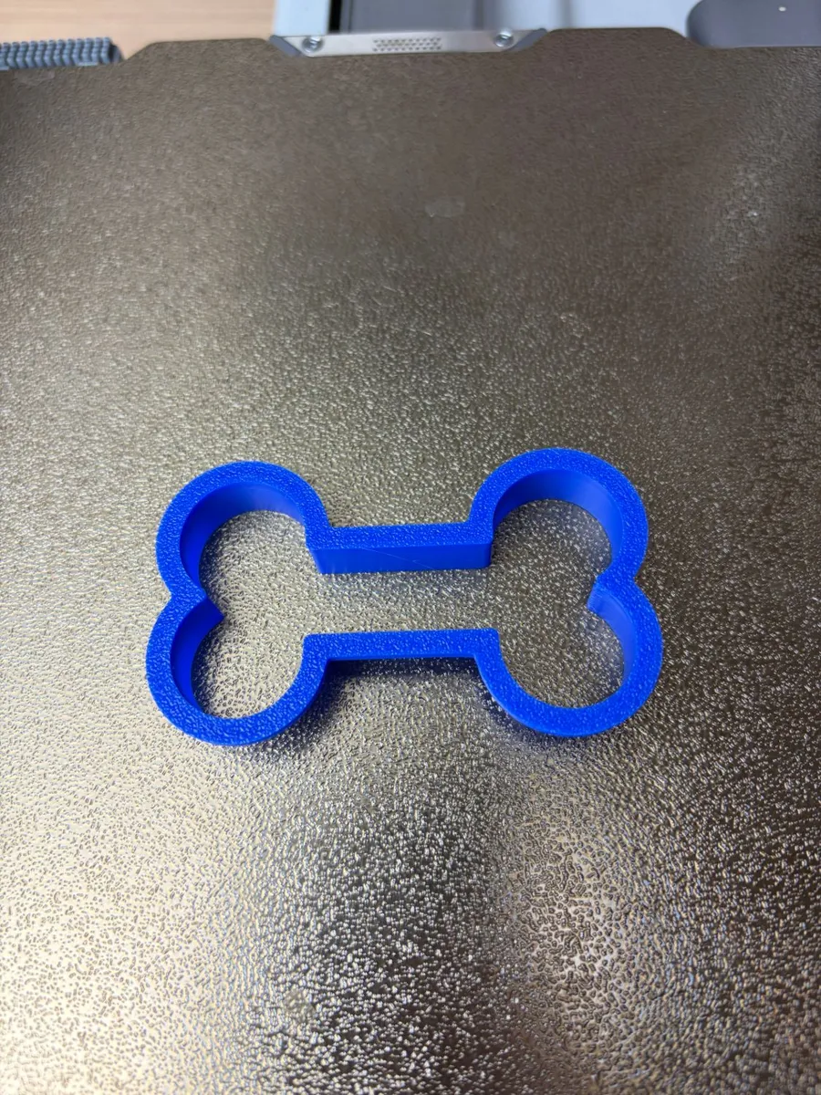 The blue 3D-printed dog bone cookie cutter on a textured print bed, just off the printer