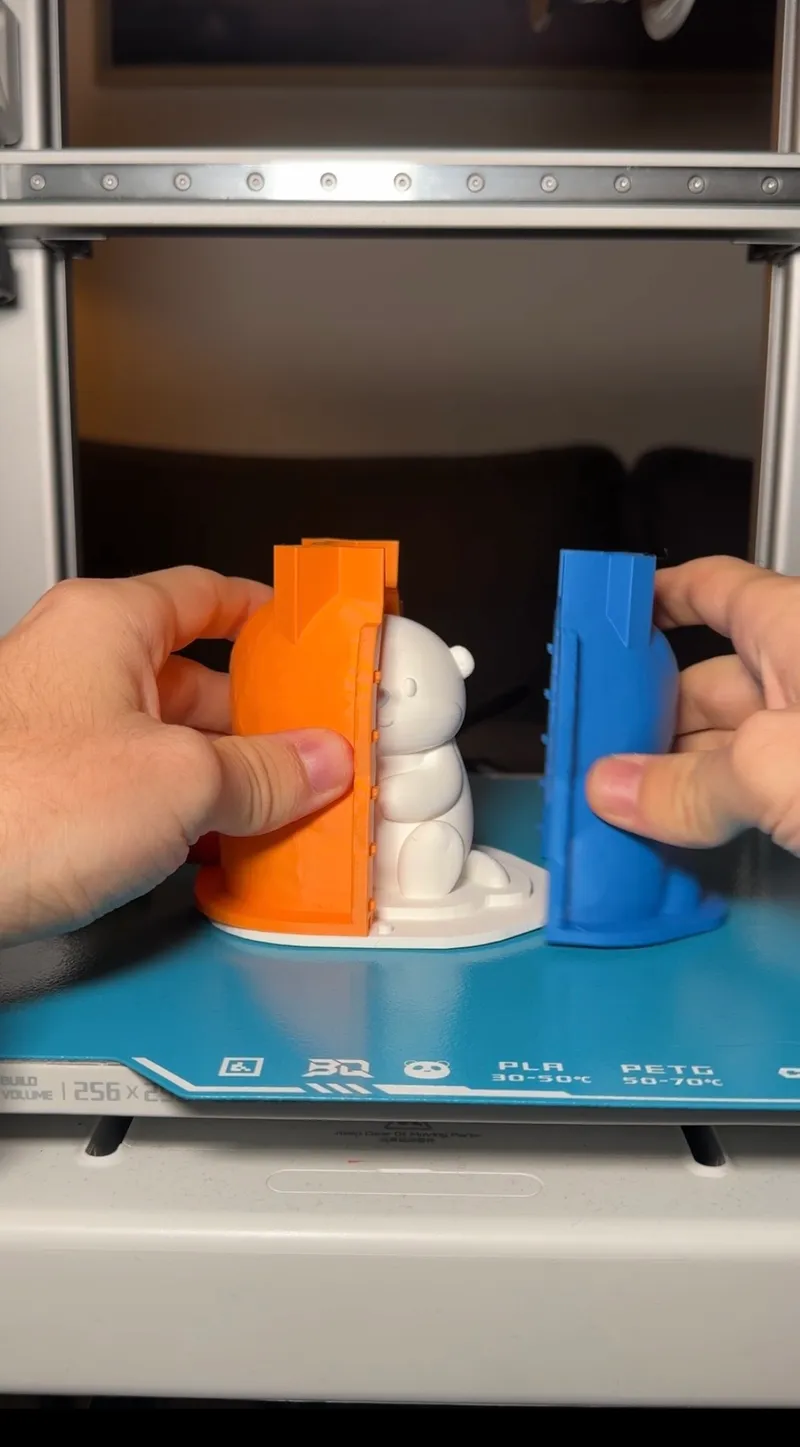 A two-part printed mold opened to reveal the white model inside, on a 3D printer bed