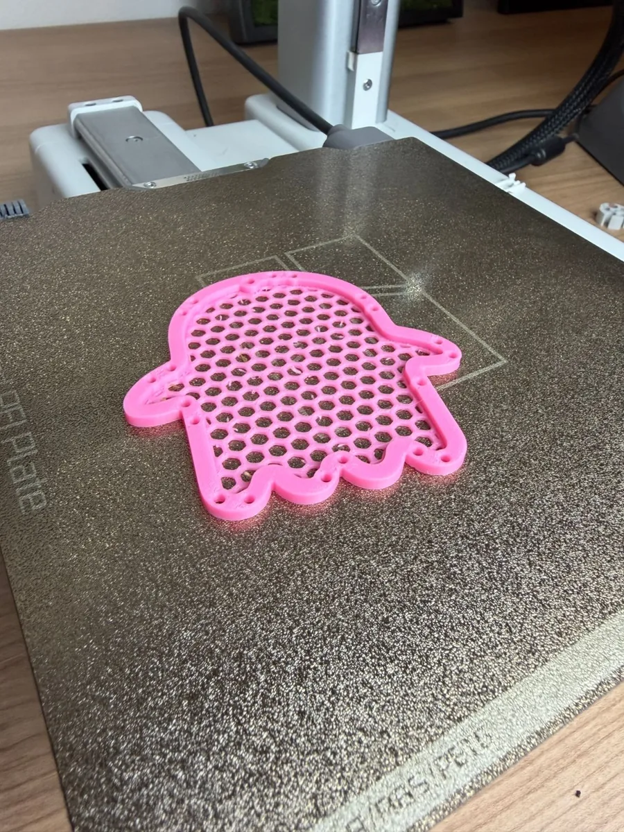 The pink mesh ghost net seen at an angle on the print bed, showing the raised rim and the honeycomb net inside it