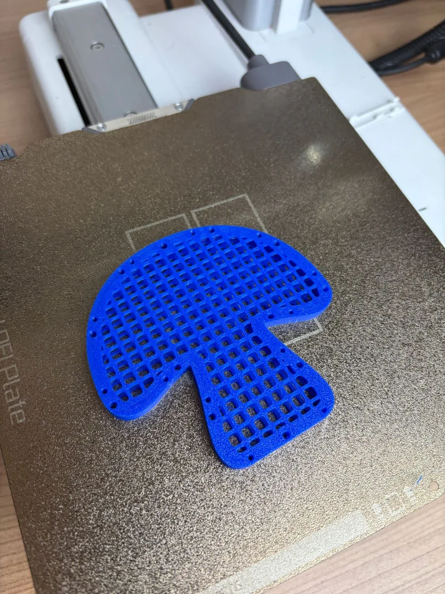 A blue mesh mushroom half after forming, its square net domed, lying on the print bed