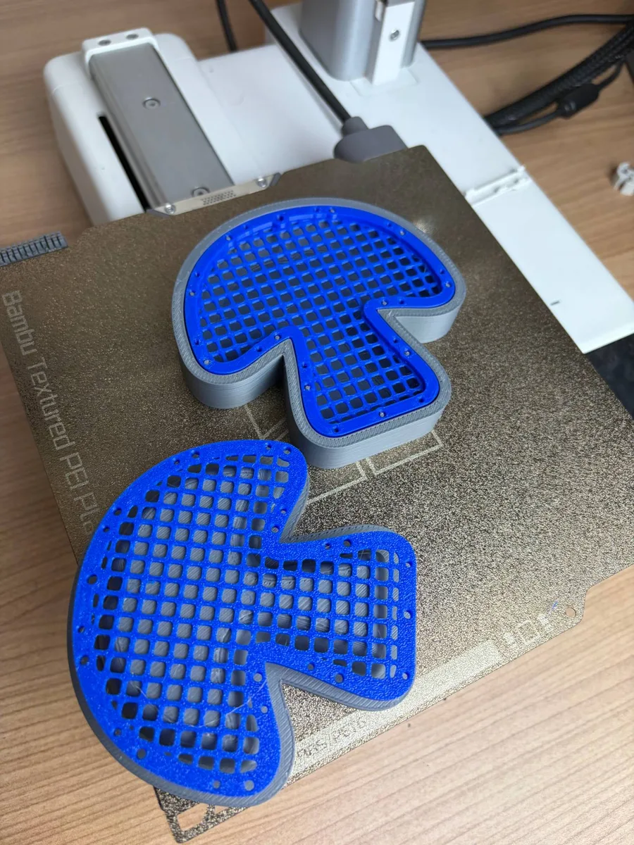 The grey printed press for the mesh mushroom on a textured print bed, a blue mushroom net seated in the cavity and a second net on the plug