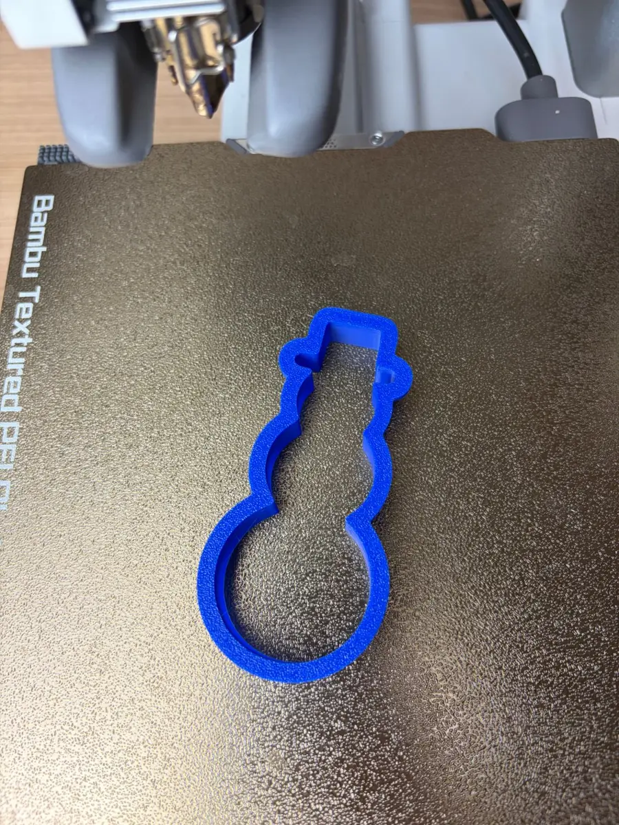 The blue 3D-printed snowman cookie cutter on a textured print bed, just off the printer
