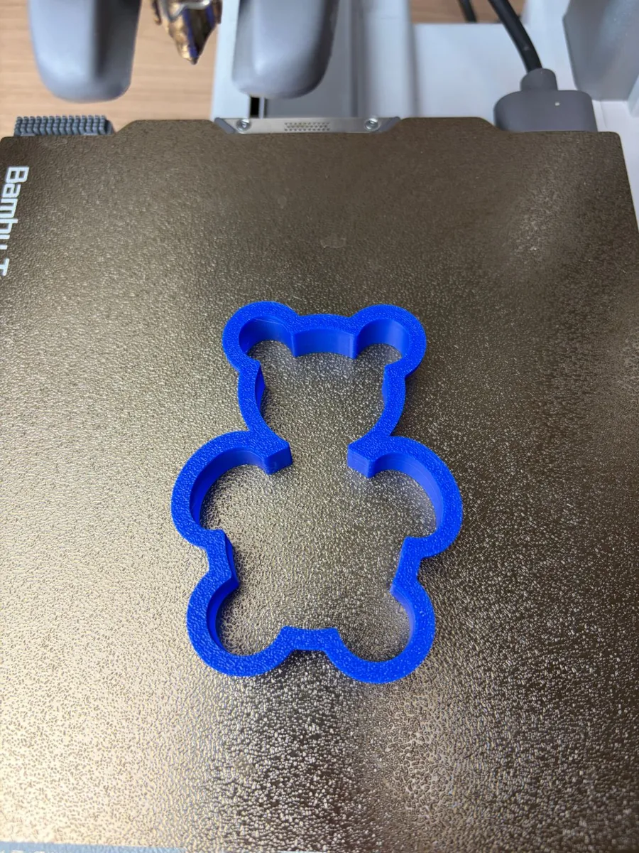 The blue 3D-printed teddy bear cookie cutter on a textured print bed, just off the printer